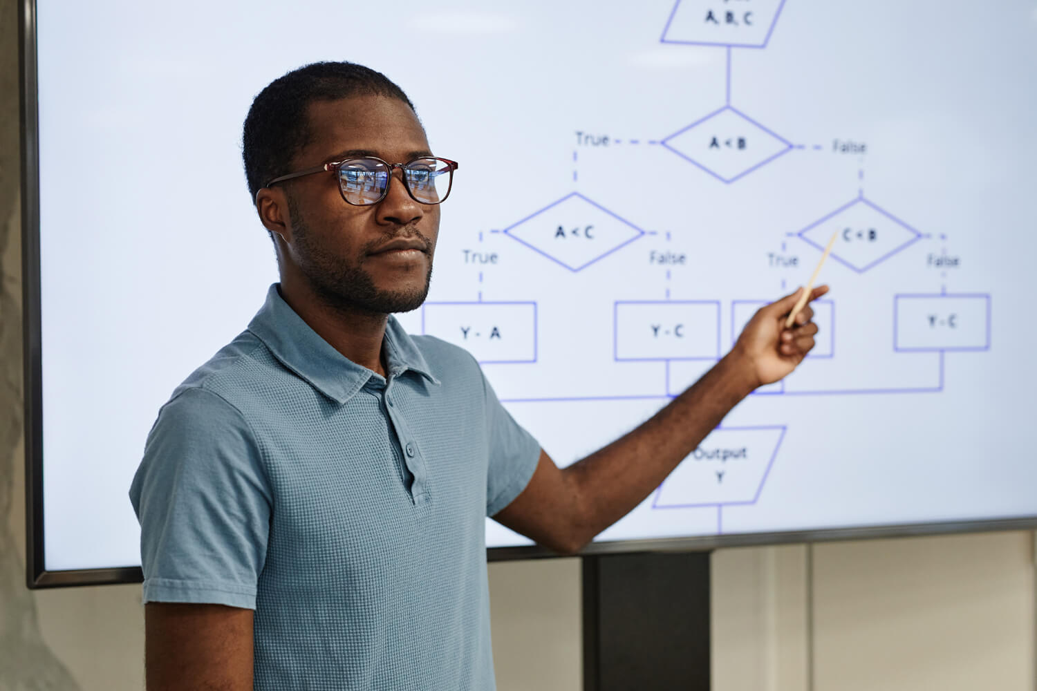 Portrait of male African-American teacher pointing at screen in coding class, copy space